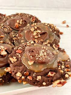 chocolate cookies with nuts and caramel drizzled on top, sitting on a white plate