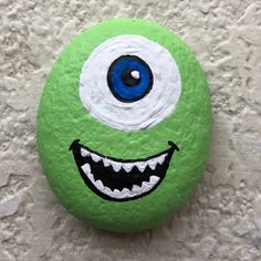 a green painted rock with an evil face and big blue eyes on it's side