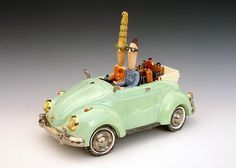 a green toy car with people riding in it's top and the roof down