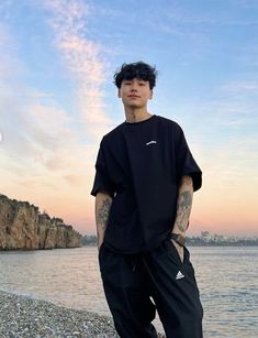 a young man standing on the beach with his hands in his pockets and looking off into the distance