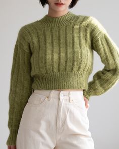 a young woman wearing a green sweater and white pants with her hands on her hips