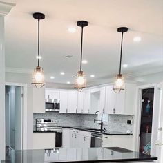 a kitchen with white cabinets and black counter tops, lights hanging from the ceiling over the island