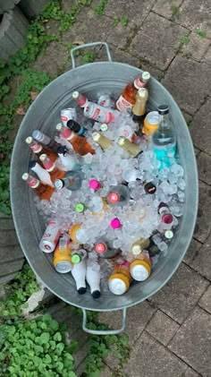 a bucket filled with lots of ice and bottles on top of a brick floor next to grass