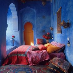 a bedroom with blue walls and red bedding in the corner is furnished with colorful pillows