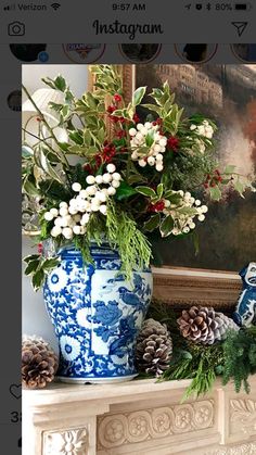 a vase with flowers and greenery sitting on a mantel in front of a painting