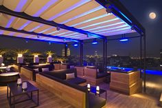 an outdoor restaurant with tables and chairs overlooking the city at night, lit up by blue lights