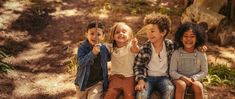 four children sitting on top of each other in the woods, laughing and making funny faces