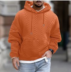 a man wearing an orange hoodie and jeans is standing in front of a building