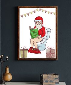 a framed christmas card featuring santa sitting on a toilet reading a book