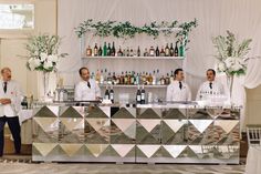 four men in white shirts and ties standing at a bar with bottles on the counter