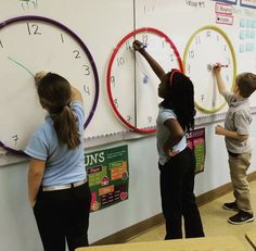 three children are writing on the wall with clocks