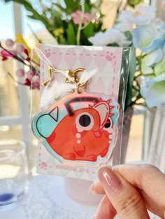 a hand holding a keychain with an orange fish in the center and pink flowers behind it