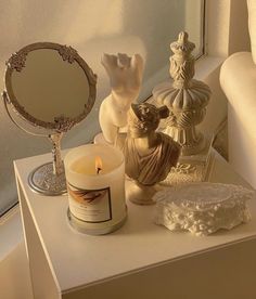 a candle sits on a table next to some figurines and an ornate mirror