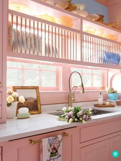 a kitchen with pink cabinets and white counter tops, gold faucets and flowers on the window sill