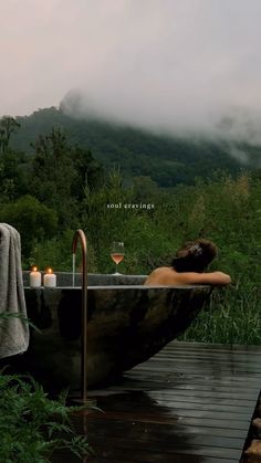 a woman sitting in a bathtub with candles on the side and mountains in the background