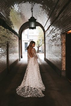 a woman in a long white dress walking down a tunnel