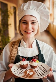 a woman in chef's outfit holding a plate with desserts on it and smiling at the camera