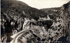 an old black and white photo of a winding road in the mountains with trees on both sides