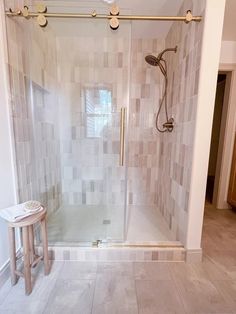 a walk in shower sitting inside of a bathroom next to a wooden stool on the floor