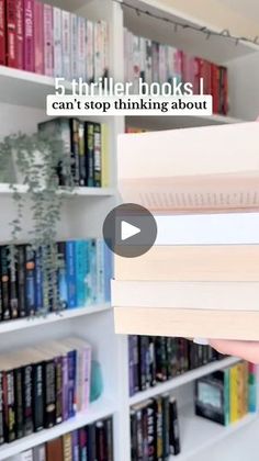 a person holding two books in front of a book shelf with many books on it