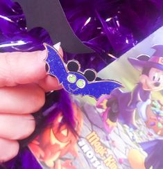 a person holding a mickey mouse pin in front of a purple box with other items