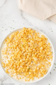 a white bowl filled with corn on top of a marble counter next to a napkin