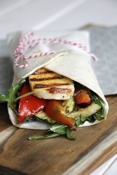 a wrap filled with meat and veggies on top of a wooden cutting board