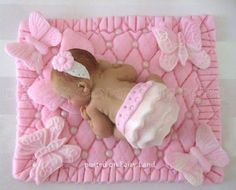 a cake shaped like a baby laying on top of a pink blanket with butterflies around it