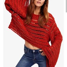 a woman wearing a red knitted sweater and jeans posing for the camera with her hands on her head