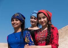 three young women standing next to each other on top of a sandy hill with blue sky in the background