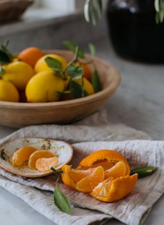 oranges and other fruit on a table with a bowl of lemons in the background