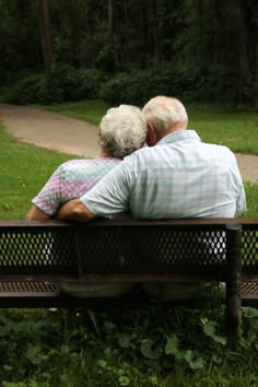 an older couple sitting on a bench in the park looking out at the grass and trees