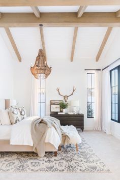 a bedroom with a bed, dresser and chandelier hanging from the ceiling in front of two windows