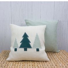 two pillows with trees on them are sitting on a wicker table next to a wooden wall