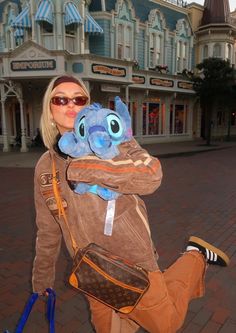 a woman holding an adorable stuffed animal in front of a shopping center with buildings behind her