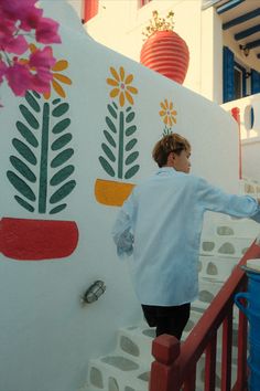 a woman in white jacket standing on steps next to wall with flowers painted on it