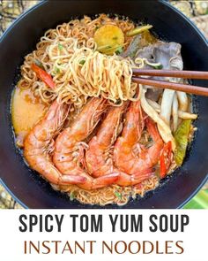 an image of spicy tom yum soup with noodles and shrimp in a black bowl