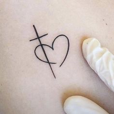 a small cross and heart tattoo on the back of a woman's ribcage