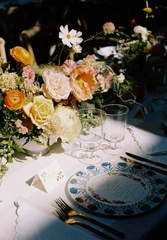 an arrangement of flowers on a table with place cards and silverware for dinner guests