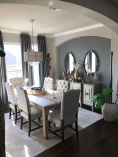 a dining room table with white chairs in front of a large window and two round mirrors on the wall