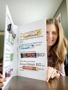 a woman sitting at a table holding up an open book with candy bars on it