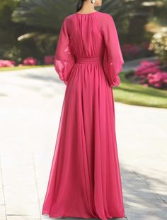 a woman in a long pink dress is standing on the sidewalk and looking off into the distance