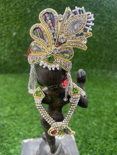 the headpiece is adorned with jewels and beads on top of a statue in front of some green grass