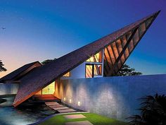 an unusual house with a triangular roof and water feature in the front yard at night