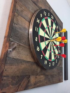 a wooden wall mounted clock with darts on it's side and arrows pointing in the opposite direction