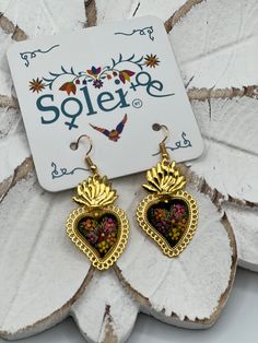 These beautiful gold plated earrings feature a hand painted floral design.  It is the perfect accessory and pop of color for your outfit! Every piece is completely unique because of the detailed process that goes into creating it.  The black lacquer is created by mixing in layers of dirt with a grease from the Cochinilla bug. The flowers are painted on with our finger tips using ground up natural pigments and linseed oil. To finish the process we apply a protective coat to conserve the painting Hand Painted Gold Dangle Jewelry, Artistic Gold Jewelry For Festive Occasions, Artistic Hand Painted Gold Earrings, Gold Hand Painted Dangle Jewelry, Heart-shaped Gold Flower Earrings As Gift, Gold Heart-shaped Flower Earrings As Gift, Bohemian Gold Heart Earrings As Gift, Gold Bohemian Heart Earrings For Gifts, Bohemian Gold Heart Drop Earrings