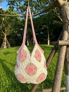 a crocheted bag hanging from a tree branch in the grass on a sunny day