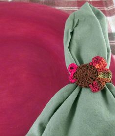 a green napkin with crocheted flowers on it sitting on a pink cloth covered table