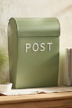 a green mailbox sitting on top of a wooden table next to a cup and book