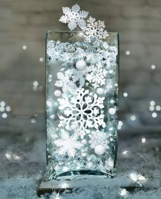 a glass vase filled with snowflakes on top of a table next to christmas lights